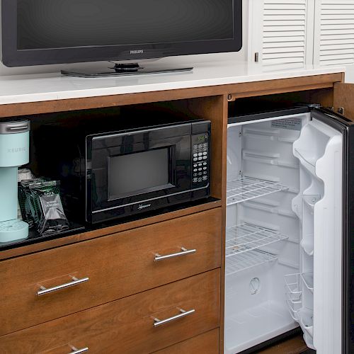 The image shows a wooden cabinet with an open refrigerator, a microwave, a coffee maker, and a television on top.